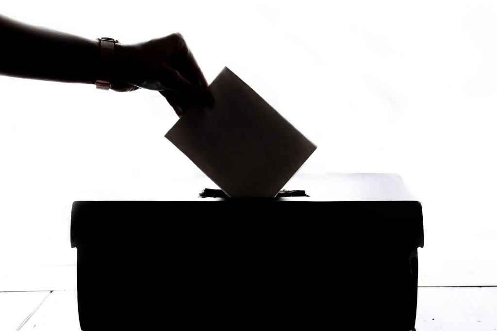 A hand dropping a ballot into a ballot box. 