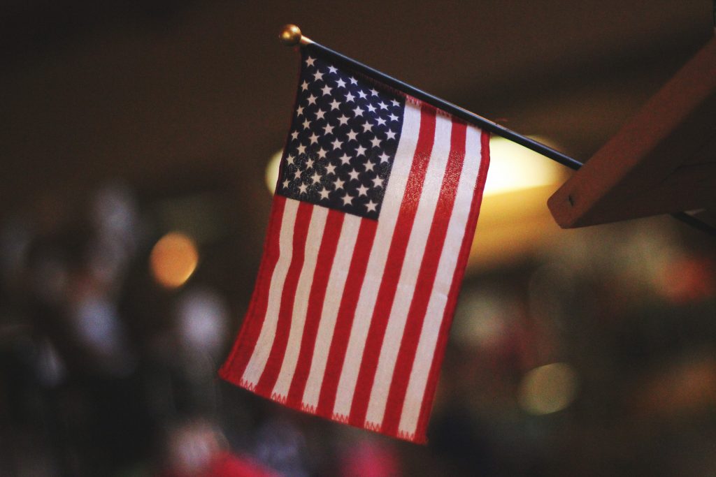 A zoomed in image of a small USA flag on a podium in front of a blurred out background. 